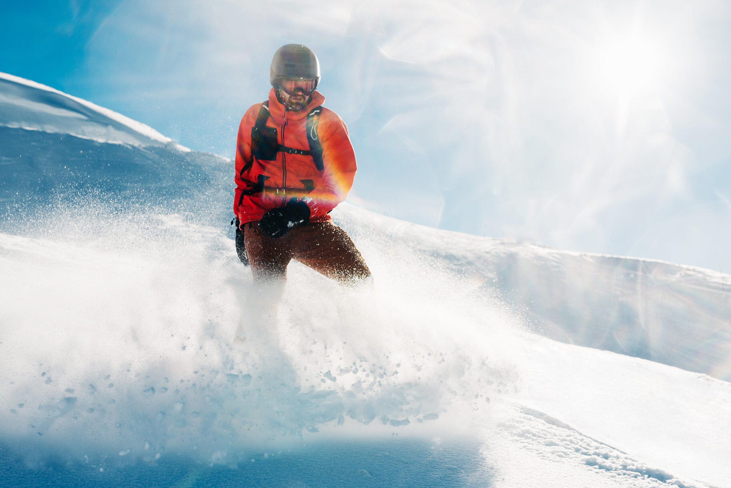 Serious snowboarder is standing in the red suit on the snow powder hill and looking into the distance